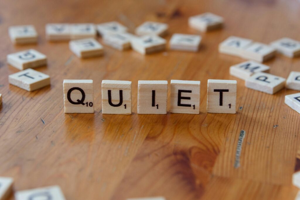 Scrabble tiles spelling 'QUIET' on a wooden surface, symbolizing calm and tranquility.
